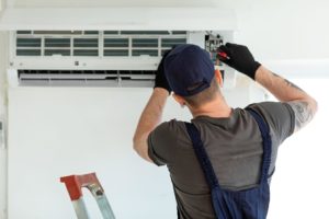 Technician performing maintenance on a commercial HVAC system, using tools while standing on a ladder, emphasizing repair and upkeep services.