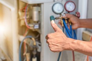 HVAC technician giving a thumbs up while checking pressure gauges on an air conditioning unit, illustrating HVAC repair and maintenance services.