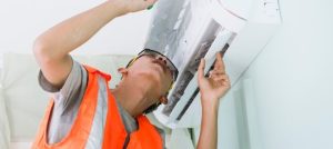 HVAC technician performing maintenance on a wall-mounted air conditioning unit, highlighting the importance of regular HVAC maintenance practices.