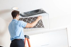 Man replacing an air duct filter while standing on a ladder, illustrating the importance of duct cleaning and HVAC maintenance.