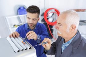 Two HVAC technicians inspecting and repairing an air conditioning unit, showcasing hands-on service and expertise in HVAC solutions.