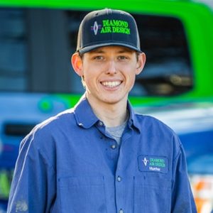 Technician from Diamond Air Design wearing branded uniform and cap, smiling in front of HVAC service vehicle.