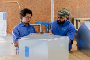 Two technicians collaborating on assembling a metal component in a workshop environment.