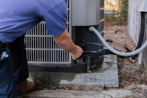 Technician servicing air conditioning unit outdoors, focusing on maintenance and repair tasks.