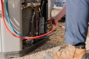 Technician servicing HVAC unit with colored refrigerant hoses in residential setting.