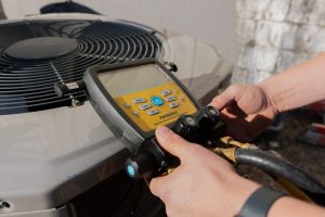Technician using a digital gauge on an outdoor air conditioning unit for HVAC service and maintenance.